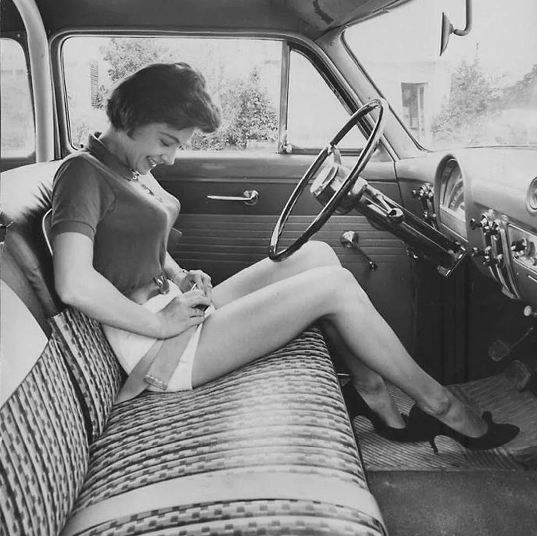 In the 1950s, a woman examines the new security belt in her car. 